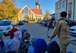 Strażak pokazuje dzieciom jak rozwija się wąż strażacki.
