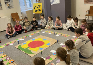 Dzieci siedzą na dywanie podczas zajęć w muzeum.