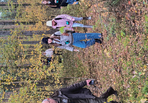 Uczniowie spacerują przez las pod okiem Pana leśniczego.