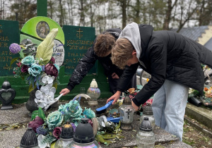 Uczniowie sprzątają na grobie zmarłych nauczycieli.