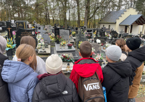 Uczniowie stoją wokół grobu zmarłych nauczycieli.