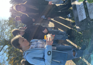 Uczniowie stawiają zapalony znicz na grobie.