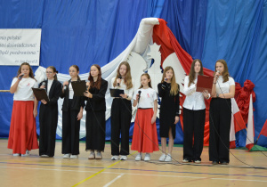 Zespół wokalny śpiewa pieśń patriotyczną.